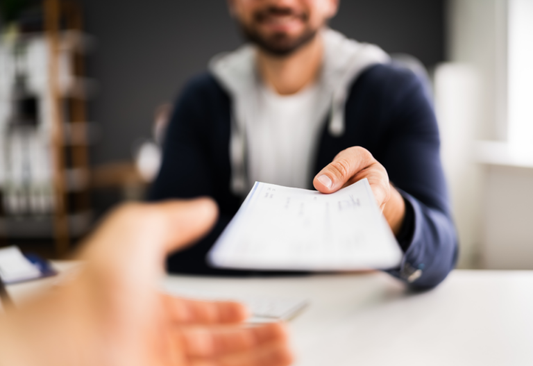 man handing another person a paycheck, the hand is outstretched and the photo is from a second person perspective