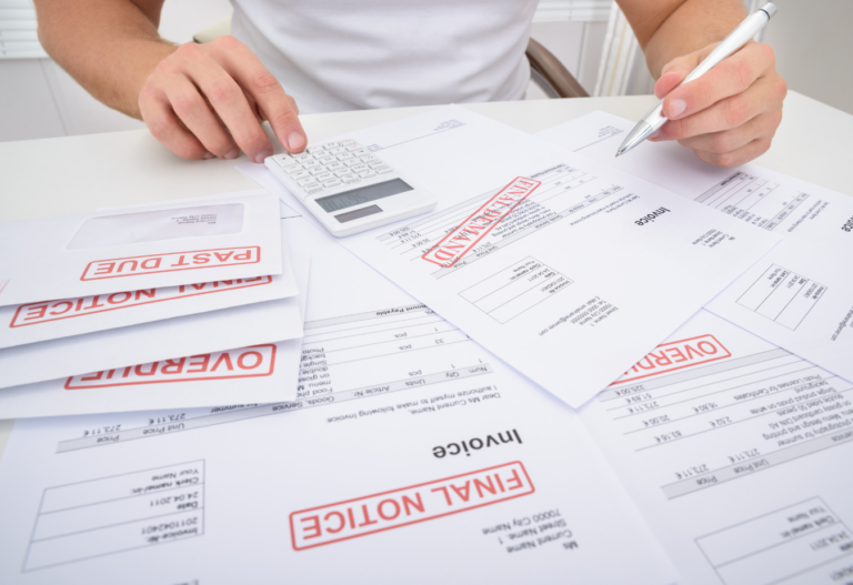 image of bills on a desk marked overdue with a calculator and a person marking with a pen